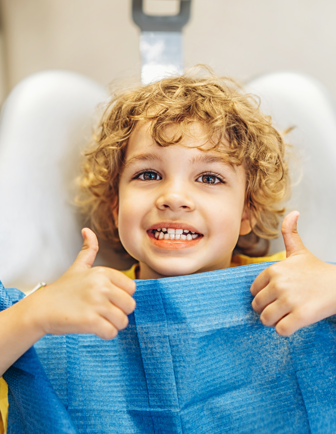 Child sitting in a dentist's chair, giving two thumbs up